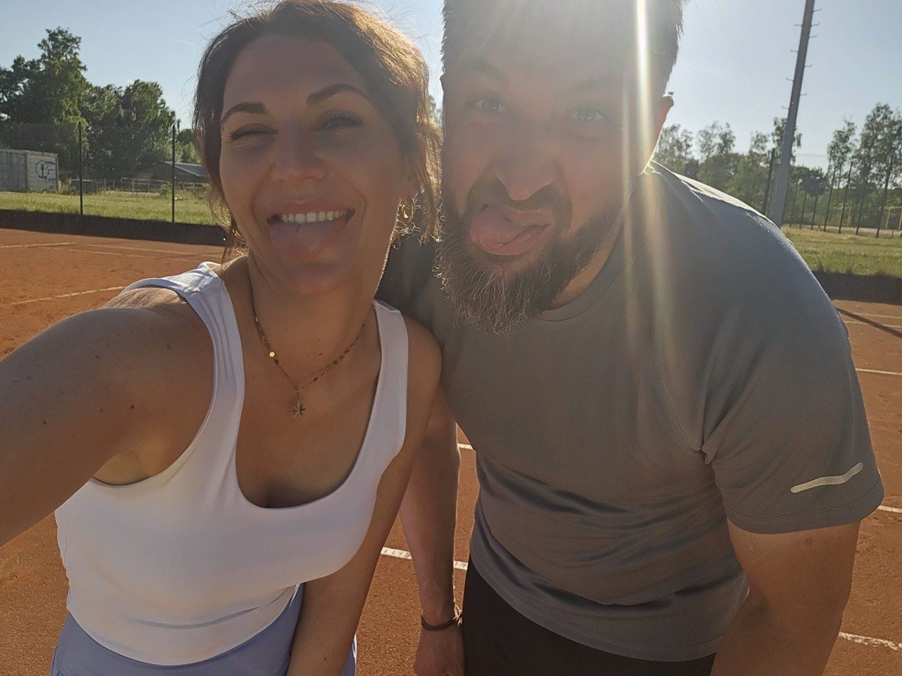 Max und Viktoria machen ein Selfie auf dem Tennisplatz und strecken die Zunge heraus